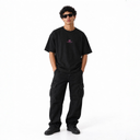 Model in sunglasses wearing the black Sinners Oversize T-Shirt from the front, styled with black cargo pants